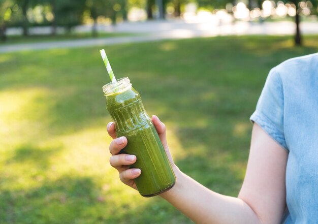 Donna che mantiene un sano frullato verde in una bottiglia di vetro