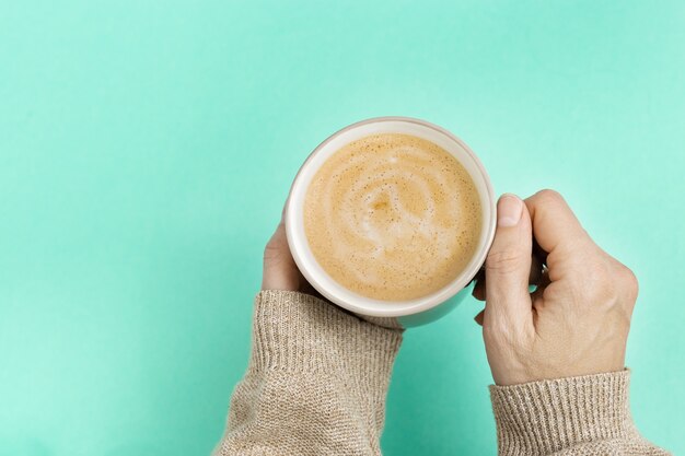 Donna che mantiene una tazza di caffè su sfondo di colore blu di tendenza.