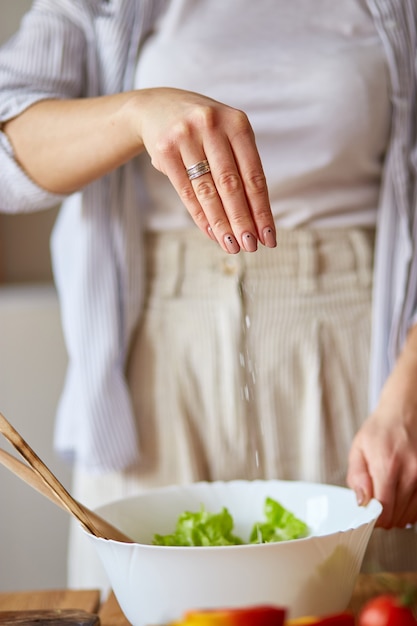 Donna che mescola foglie di insalata e verdure in una ciotola bianca