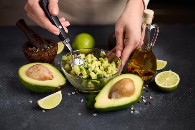 Donna che mescola frutta di avocado tagliata a fette con succo di lime e specie in una ciotola di vetro a casa