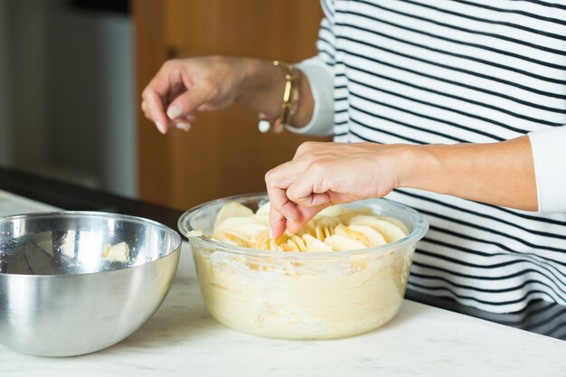 Donna che mette le mele mentre cucina la torta di mele nella cucina moderna