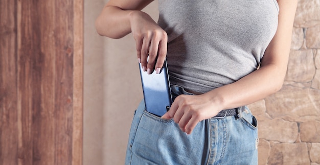 Donna che mette smartphone in tasca dei jeans.