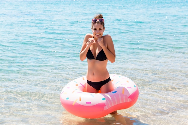Donna che nuota con una ciambella gonfiabile in costume da bagno bikini nero a braccia incrociate freddo e tremante in piedi in acqua di mare Vacanze estive e concetto di vacanza.