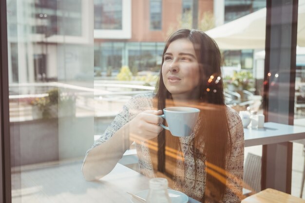 Donna che osserva attraverso la finestra con caffè