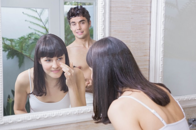 Donna che osserva nello specchio del bagno e uomo che la guarda