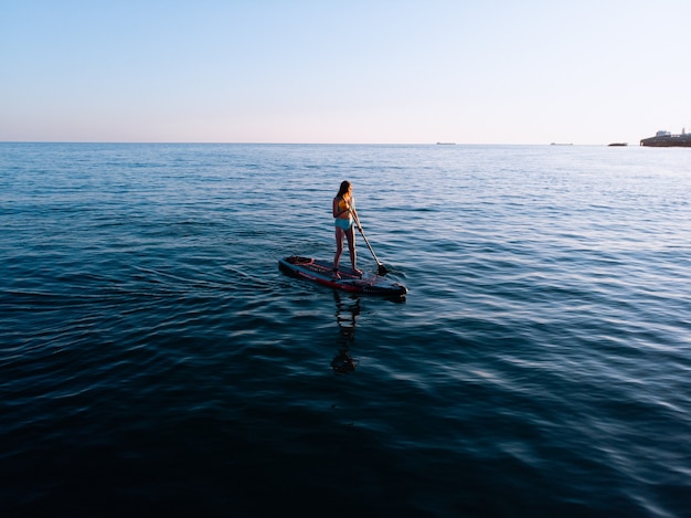 Donna che pagaia sulla tavola del sup e gode dell'acqua trasparente turchese.