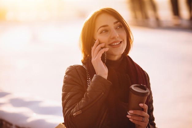 Donna che parla al telefono bere caffè fuori in inverno