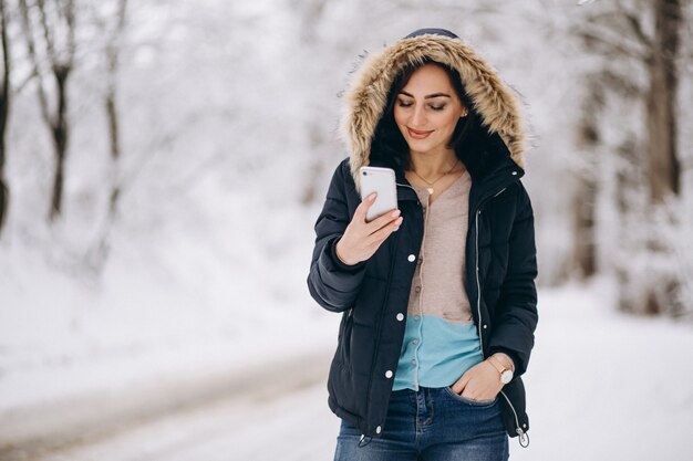 Donna che parla al telefono fuori nella foresta di inverno