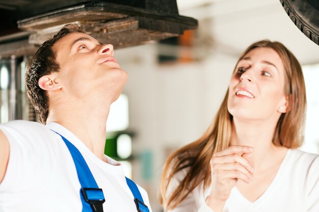 Donna che parla con meccanico di automobile nell'officina riparazioni