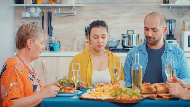 Donna che parla durante la cena. Multi generazione, quattro persone, due coppie felici che discutono e mangiano durante un pasto gourmet, godendosi il tempo a casa, in cucina seduti al tavolo.