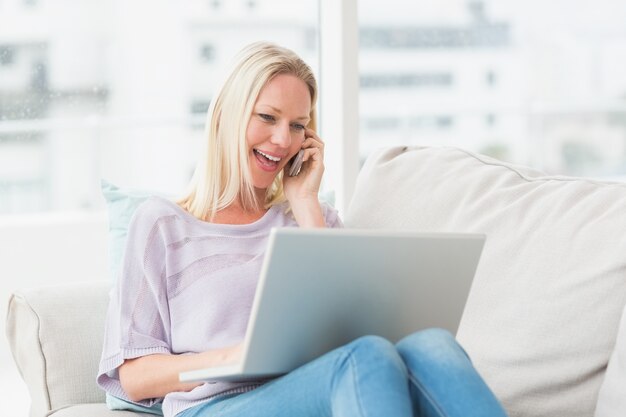 Donna che parla sul telefono mentre si utilizza il portatile sul divano