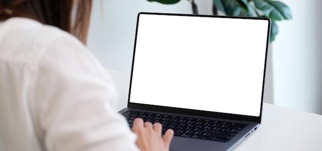 Donna che per mezzo del computer portatile con lo schermo in bianco per derisione sul fondo del modello