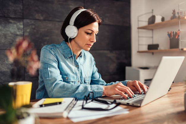 Donna che per mezzo del computer portatile e della musica d'ascolto sulle cuffie