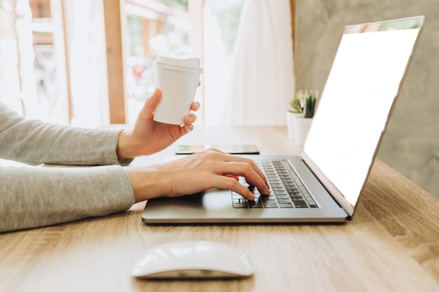 Donna che per mezzo del computer portatile e tenendo caffè che lavora alla tavola di legno