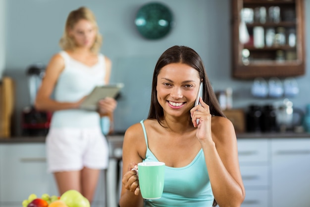 Donna che per mezzo del telefono cellulare mentre mangiando caffè a casa