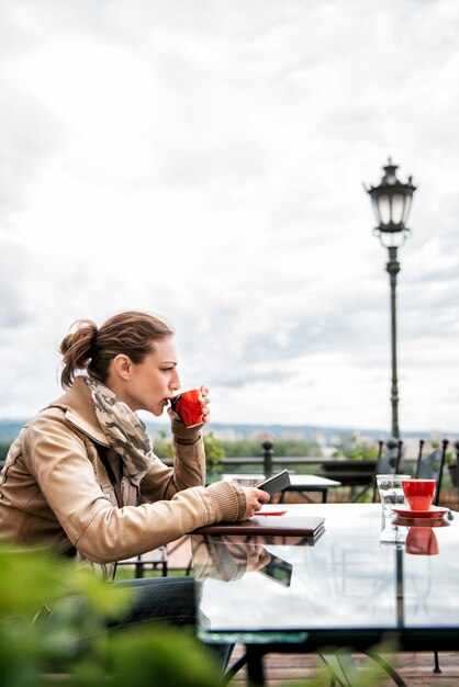 Donna che per mezzo dello Smart Phone e bevendo caffè