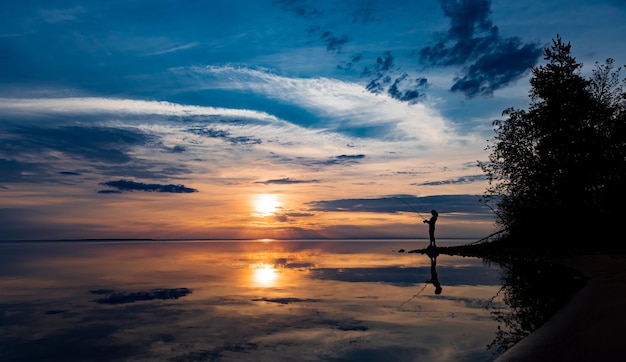 Donna che pesca sulla canna da pesca che gira al tramonto sullo sfondo