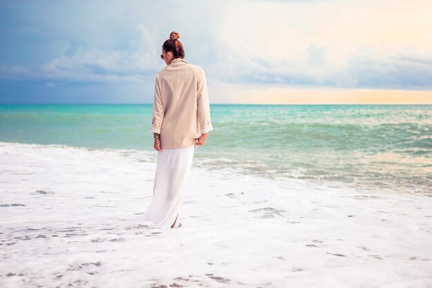 Donna che pone sulla spiaggia godendo le vacanze estive guardando il mare