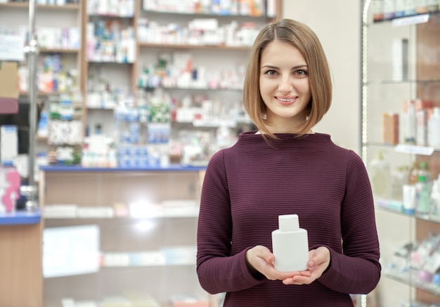 Donna che posa nella farmacia con la bottiglia cosmetica bianca.