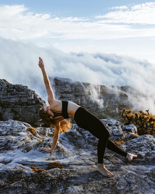 Donna che pratica lo yoga su una formazione rocciosa contro il cielo durante il tramonto