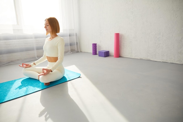 Donna che pratica yoga e meditazione in postura di loto sul tappetino da yoga rilassata con gli occhi chiusi