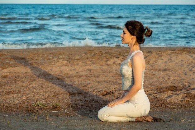 Donna che pratica yoga fuori nella posa del loto sulla spiaggia