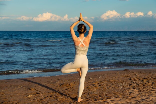 Donna che pratica yoga fuori nella posa dell'albero sulla spiaggia