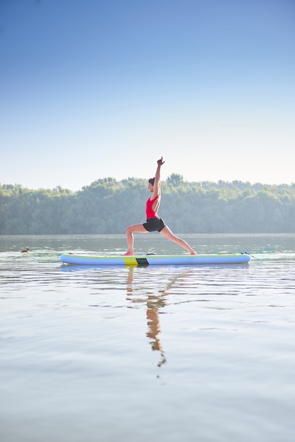 Donna che pratica yoga in una posizione di guerriero sul paddleboard