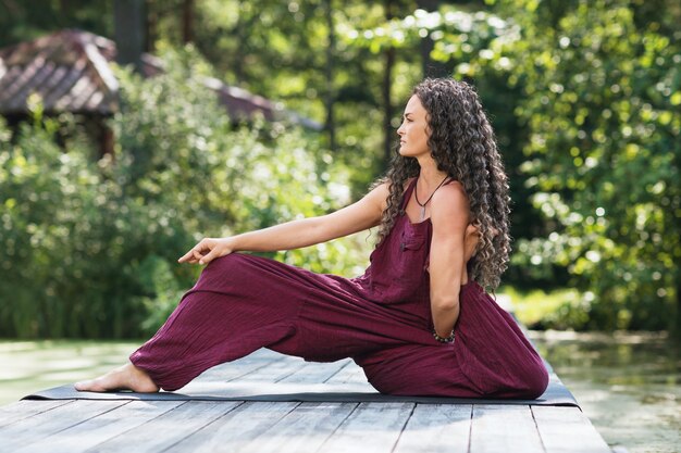 Donna che pratica yoga seduta su una stuoia nel parco in una mattina di sole e che esegue una variazione di