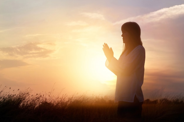 Donna che prega e che pratica meditando sul fondo di tramonto della natura, concetto di speranza