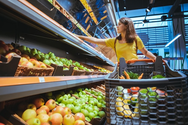 Donna che prende le mele dallo scaffale di un supermercato