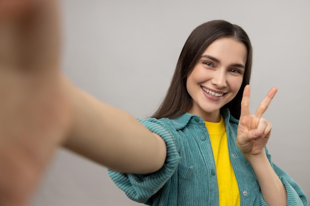 Donna che prende selfie POV flirtando esprimendo emozioni positive mostrando il gesto di vittoria del segno v