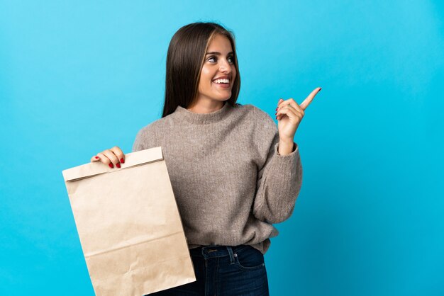 Donna che prende un sacchetto di cibo da asporto isolato sull'azzurro che intende realizzare la soluzione mentre solleva un dito