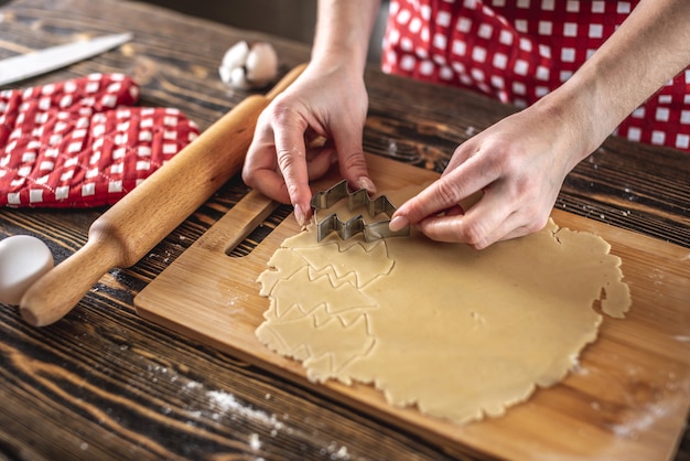 Donna che produce deliziosi biscotti fatti in casa a forma di albero di Natale nella sua cucina