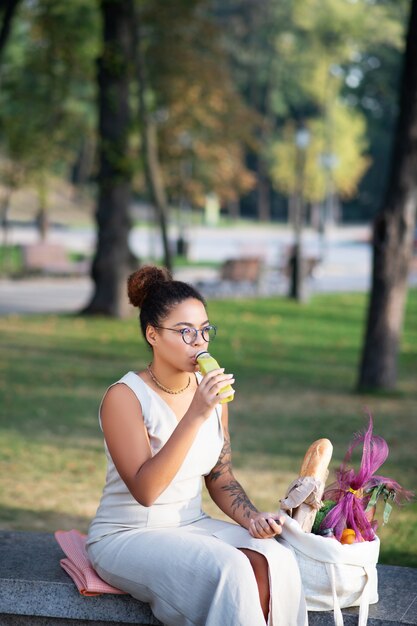 Donna che prova il frullato. Donna dalla carnagione scura con gli occhiali che prova il frullato dopo essere andata al supermercato