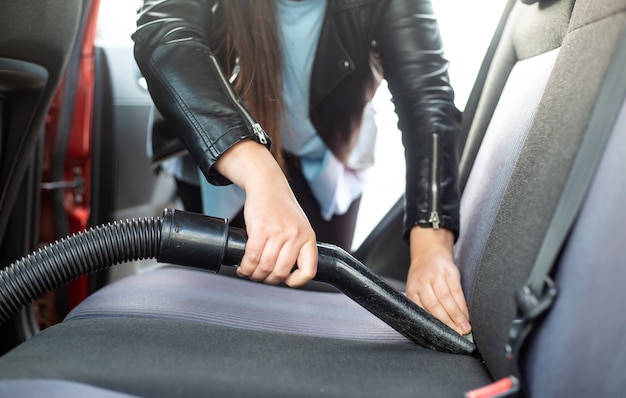 Donna che pulisce, aspira l'interno dell'auto dall'aspirapolvere, concetto di trasporto