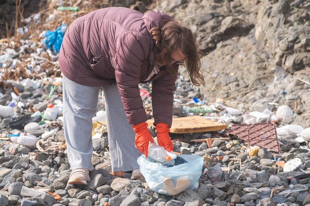 Donna che pulisce i rifiuti di plastica sulla spiaggia promuovendo la sostenibilità e il riciclaggio dei rifiuti di conservazione