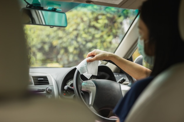 Donna che pulisce il volante con un panno umido in una pandemia di coronavirus per auto