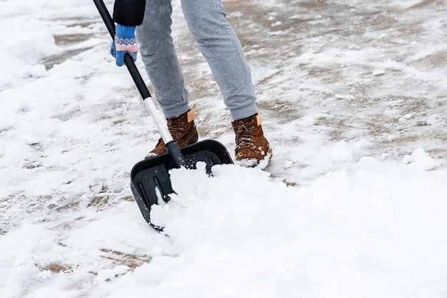 Donna che pulisce la neve dal marciapiede e usa la pala da neve.