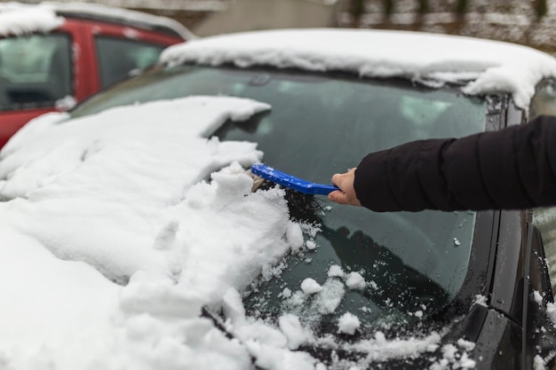 donna che pulisce la neve dall'auto con la spazzola