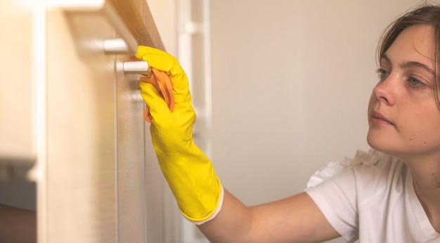 Donna che pulisce le ante dell'armadio da cucina all'interno di casa, vista ravvicinata