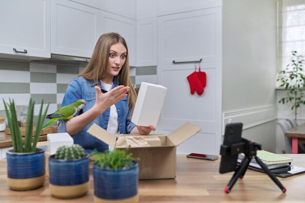 Donna che registra video su smartphone che disimballa la scatola di cartone Pappagallo domestico che aiuta a disimballare