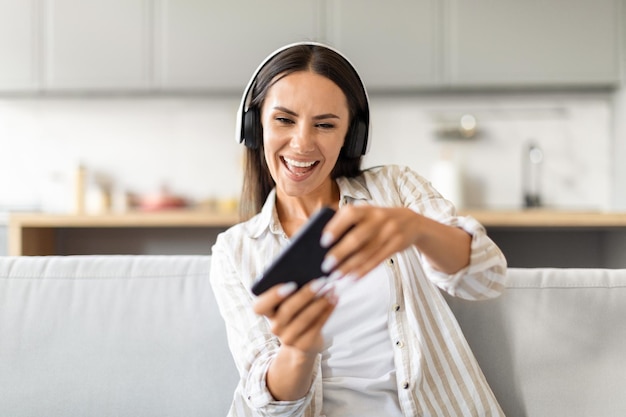 Donna che ride con le cuffie e il telefono che gioca a videogiochi