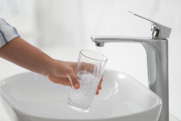 Donna che riempie il vetro con acqua dal rubinetto sopra il primo piano del lavandino