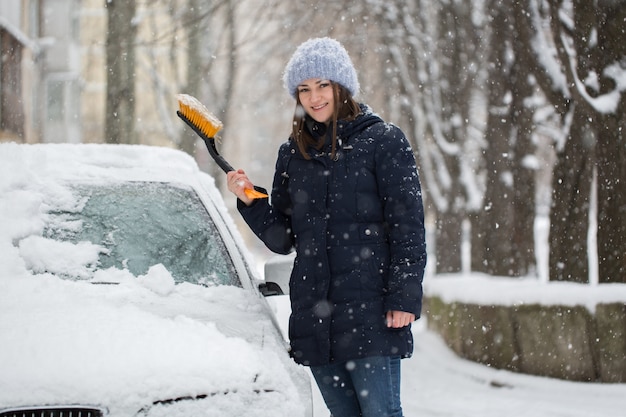 Donna che rimuove la neve dal parabrezza dell'auto