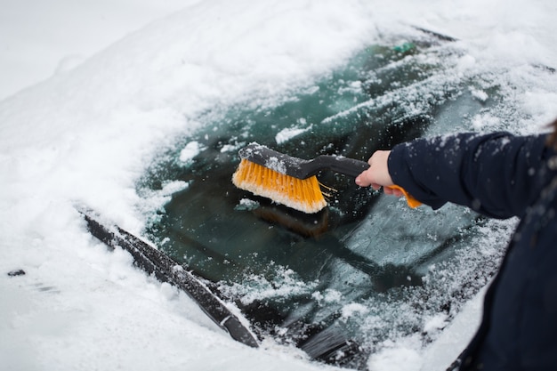 Donna che rimuove la neve dal parabrezza dell'auto