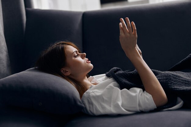 Donna che riposa sdraiata sul divano con un telefono cellulare in mano e una maglietta bianca
