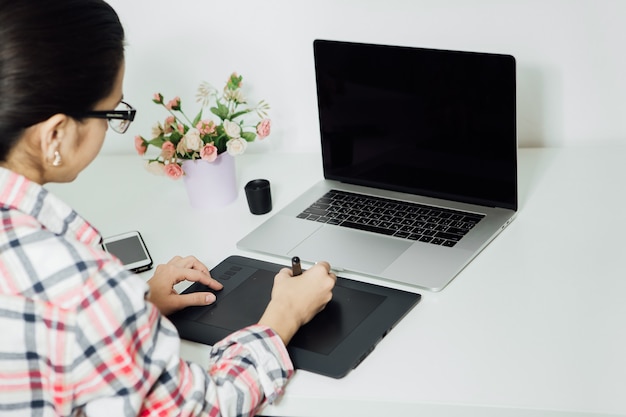 Donna che ritocca sul computer portatile utilizzando la tavoletta digitale e la penna stilo