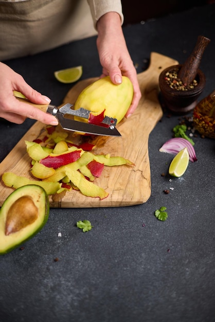 Donna che sbuccia il mango su una tavola da taglio in legno nella cucina domestica