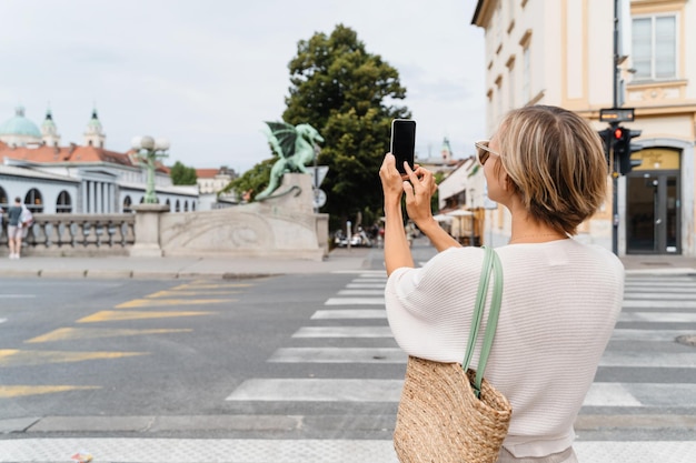 Donna che scatta una foto con lo smartphone del ponte del drago Zmajski, il più simbolo di Ljubljana, in Slovenia
